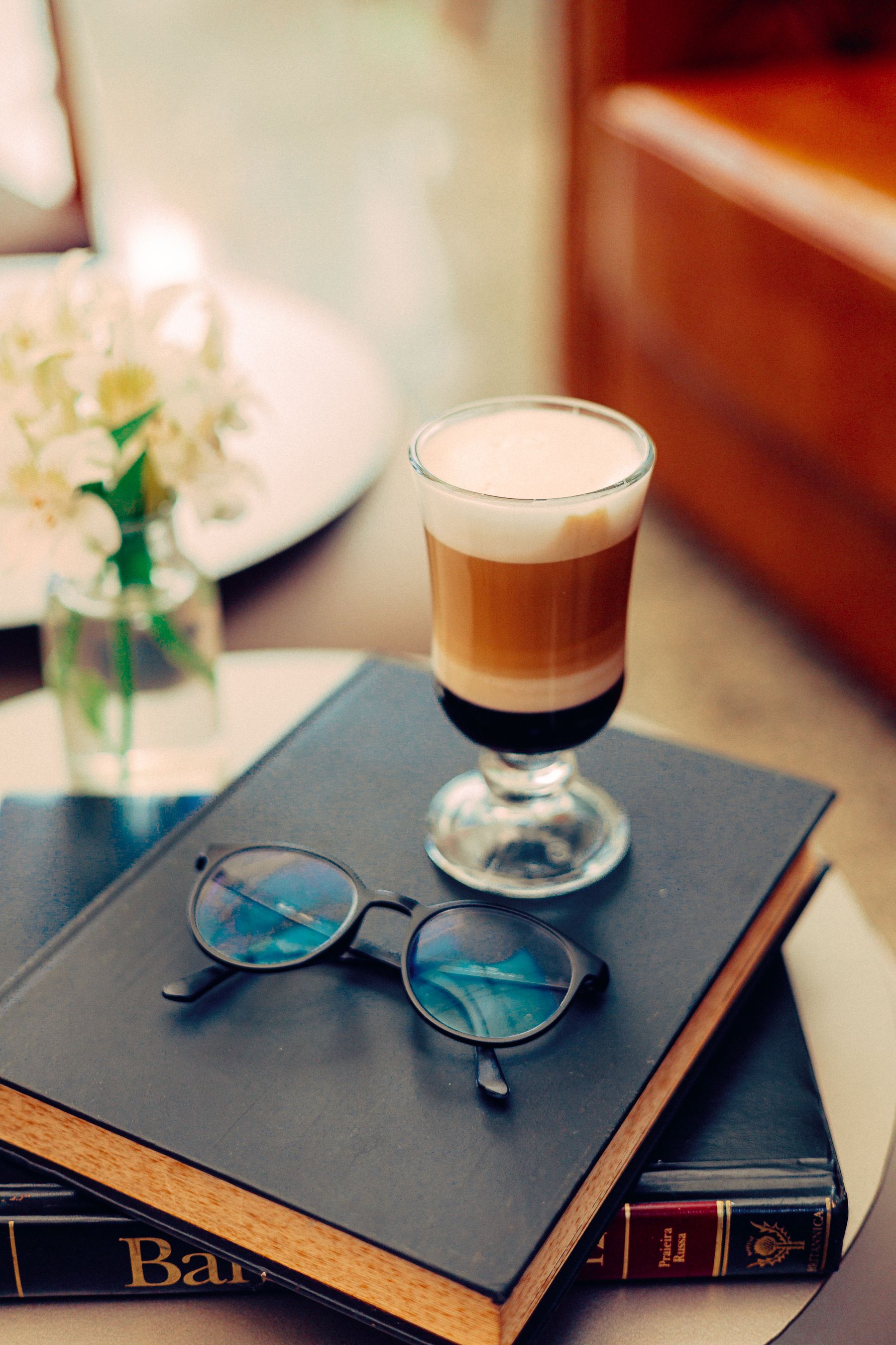 A latte and glasses resting on a stack of books, a quiet study moment.